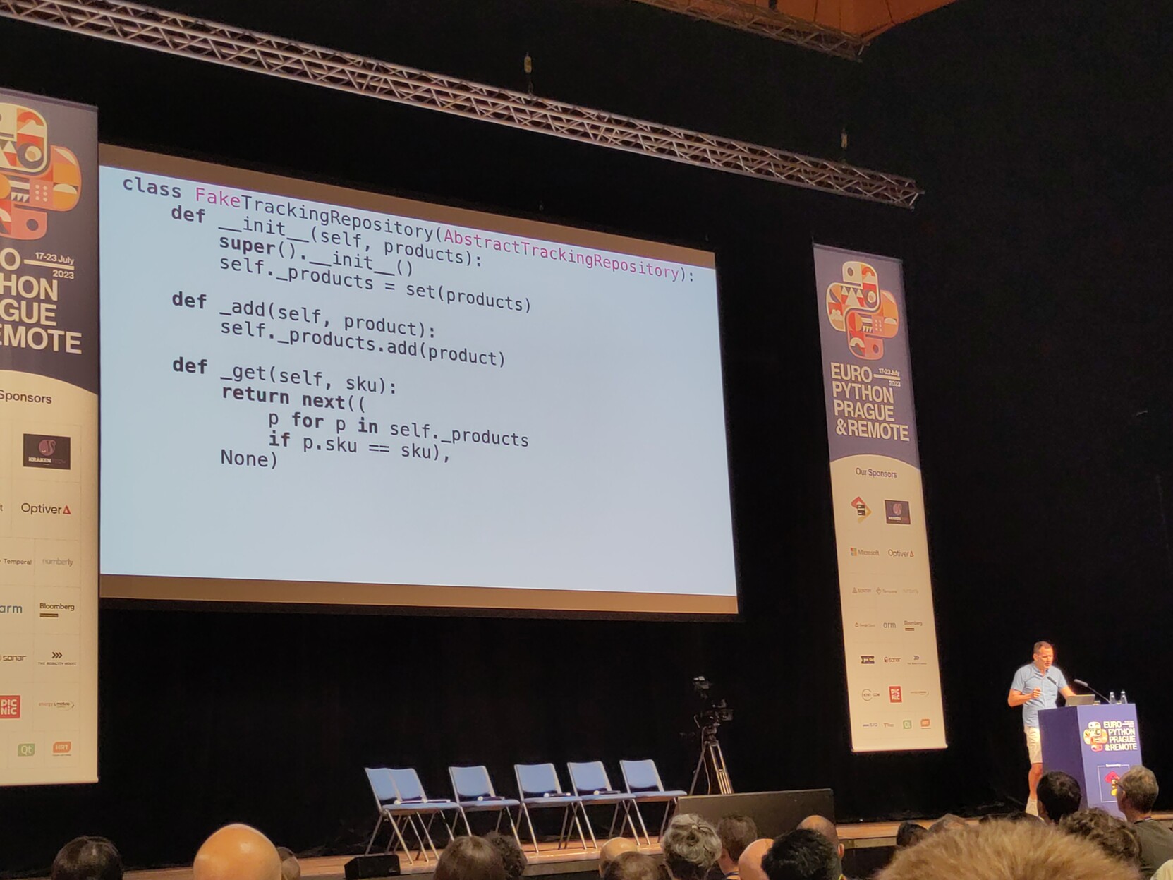 Photo of a man standing next to a big screen showing some Python code