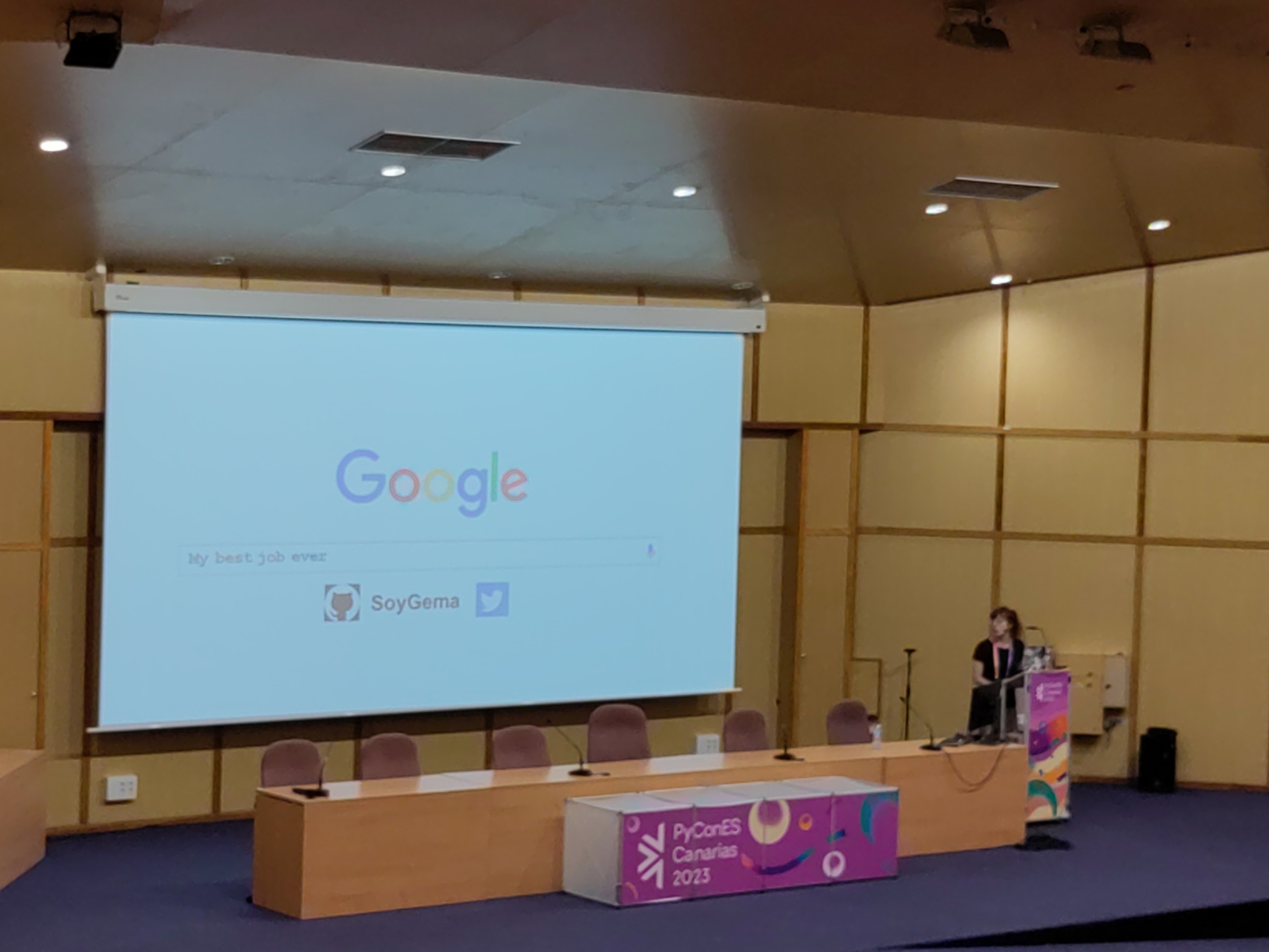 Foto de una mujer dando una charla junto a una pantalla gigante con el logo de Google