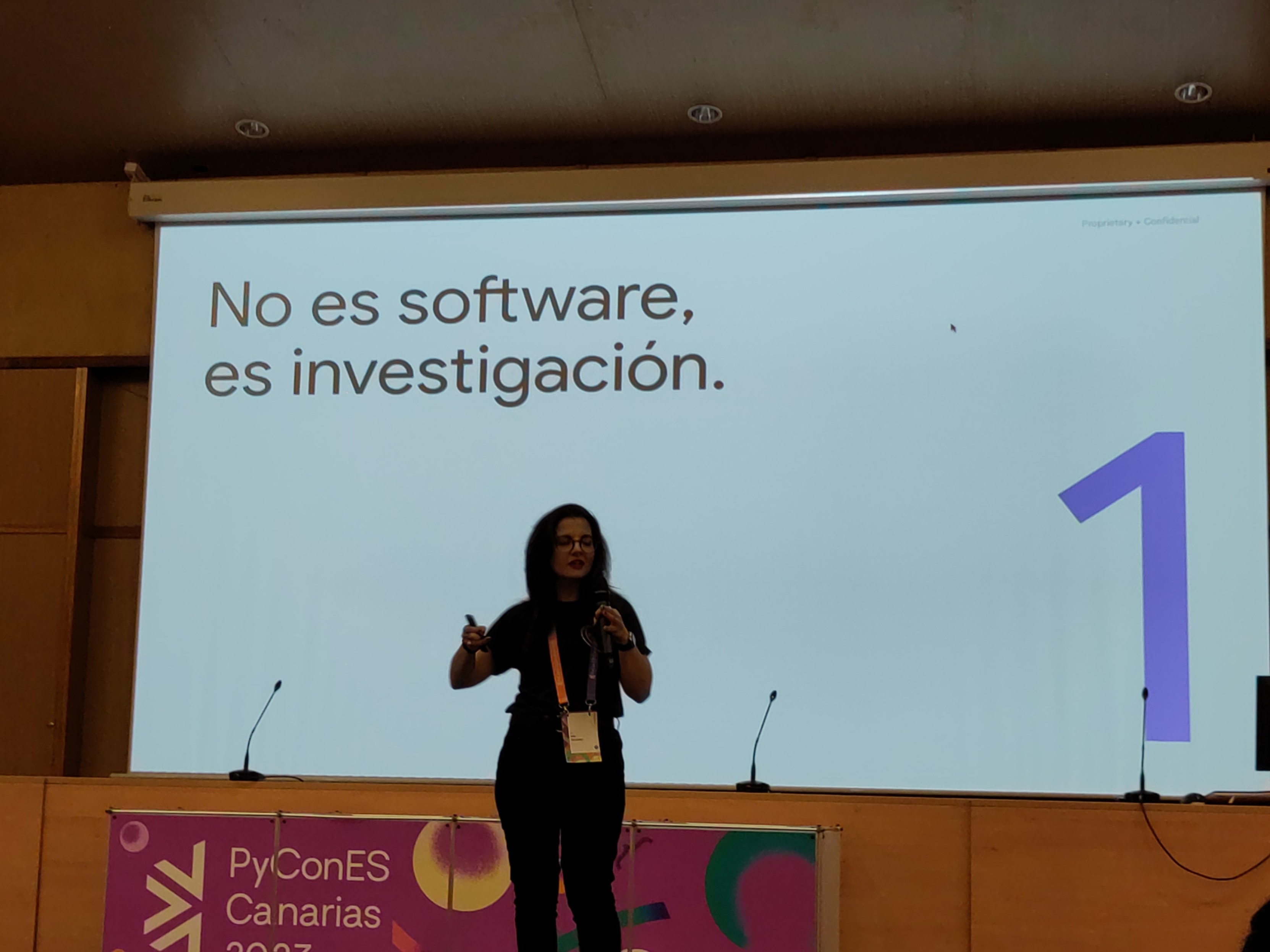 Foto de una mujer dando una charla frente a una pantalla gigante 