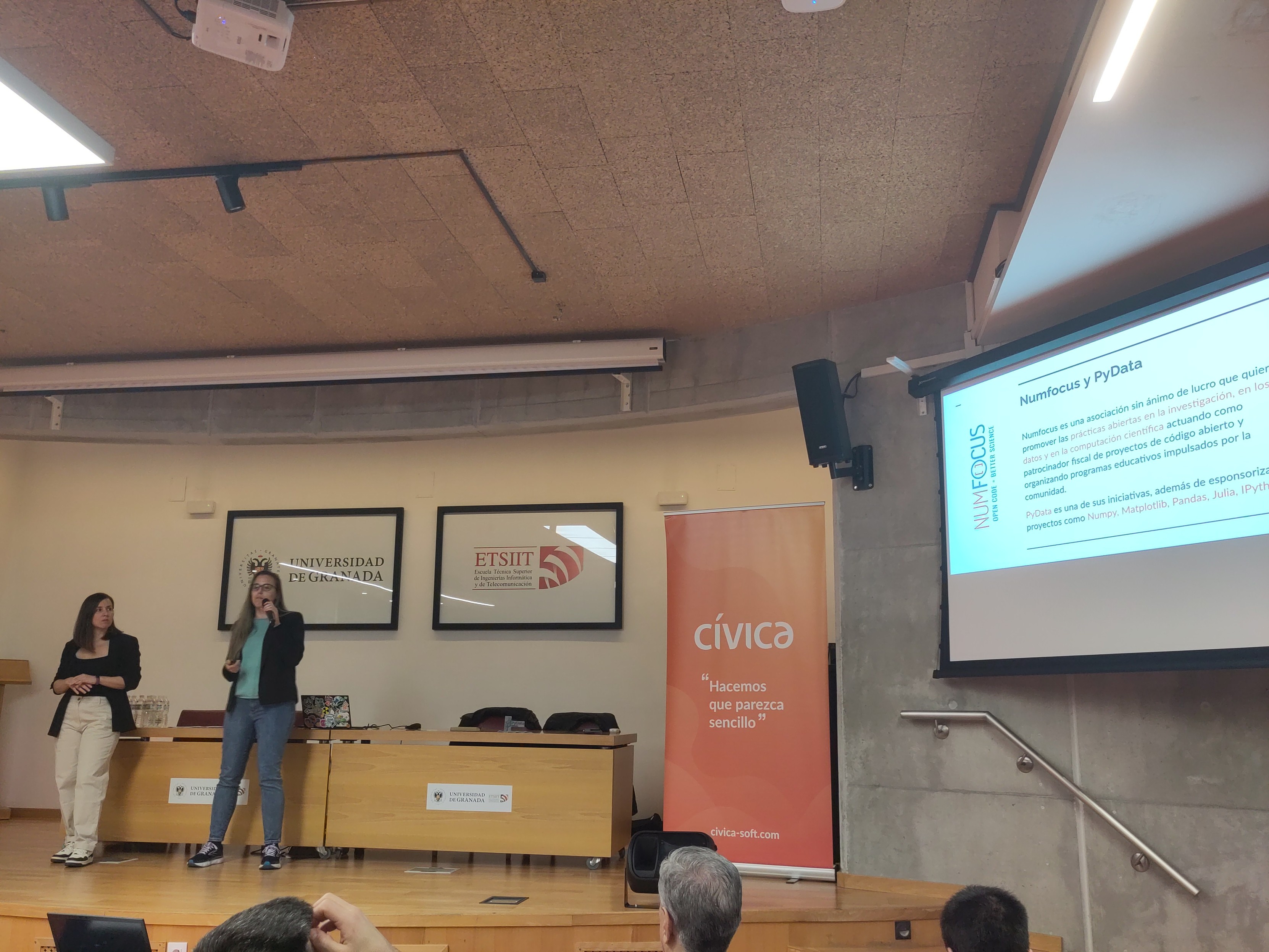 Foto de dos mujeres en un escenario presentando junto a una pantalla
